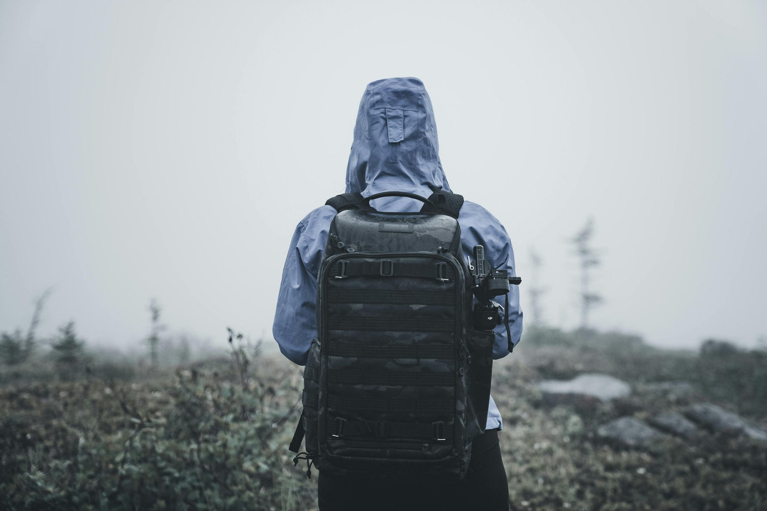 Hooded adventurer carrying a tactical MOLLE backpack in misty terrain