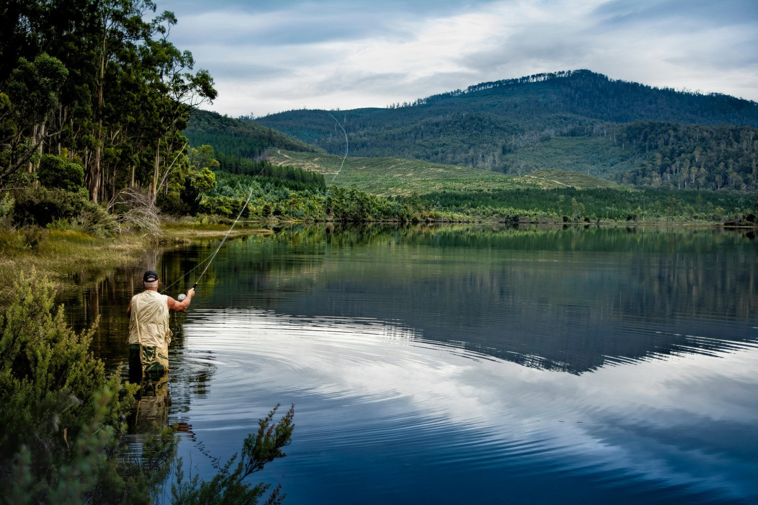 Angler casting a fly rod on a mirror-calm lake