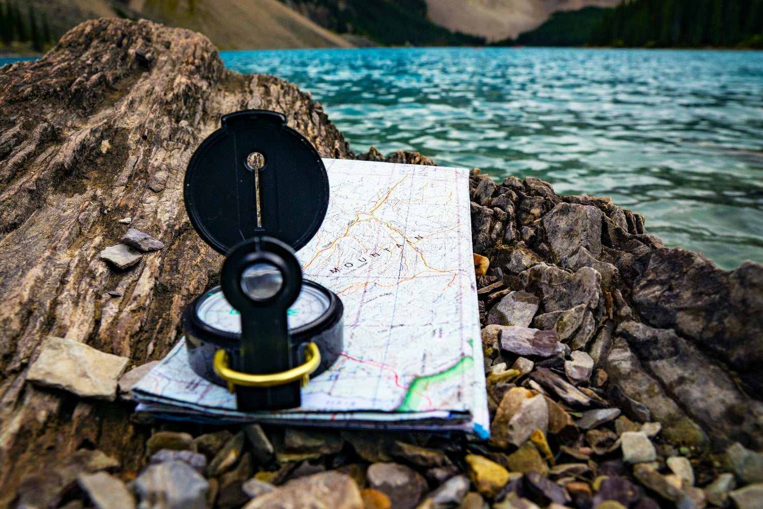 Open compass resting on a topographic map beside an alpine lake