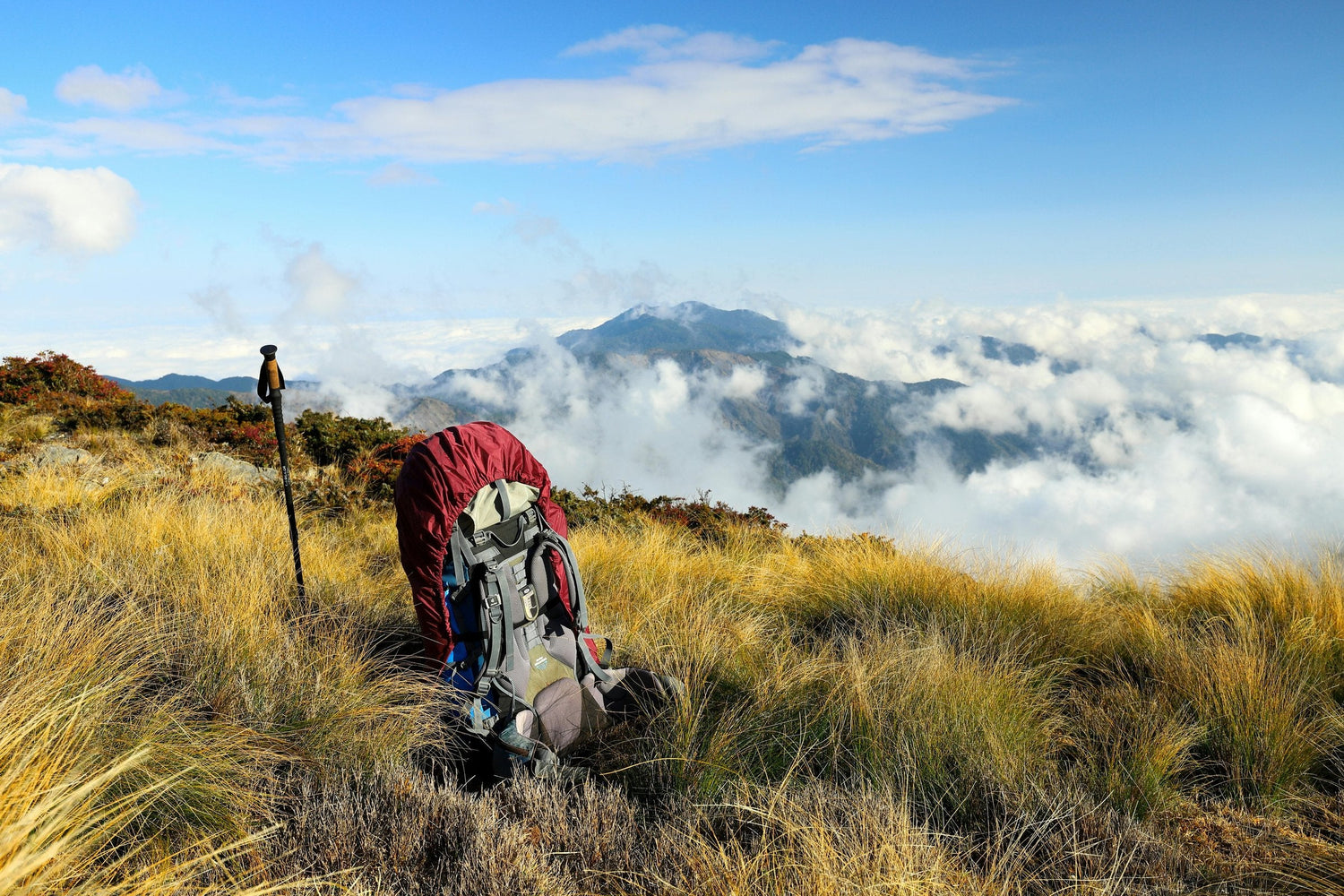 Trekking poles and backpack planted on a high alpine ridge above the clouds