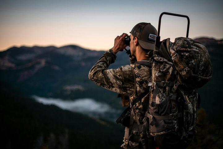 Hunter glassing the field through binoculars at dusk